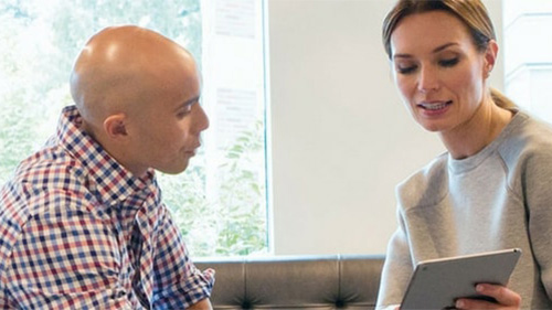 text: Woman with tablet presenting to man